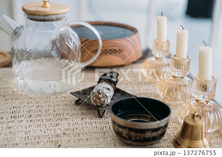 Tea meditation. Spiritual yoga tool. White candles for incense glass teapot bowl preparing for sound bell therapy placed creating oriental atmosphere. Tea meditation. Spiritual yoga tool. White candles for incense glass teapot bowl preparing for sound bell therapy placed creating oriental atmosphere. 137276755