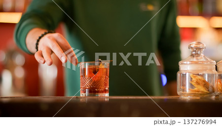 Garnishing beverage. Cocktail recipe. Barkeeper adding olive skewer to alcoholic refreshing drink. Aromatic negroni with tangerine peel. 137276994