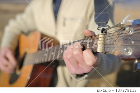 A man plays the guitar, close-up, focus on the hand and neck of the guitar. An authentic guitarist is playing outside. The concept of relaxation and leisure A man plays the guitar, close-up, focus on the hand and neck of the guitar. An authentic guitarist is playing outside. The concept of relaxation and leisure 137278115