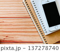 木のテーブルの上に置かれたスマートフォンと二冊のノート 137278740