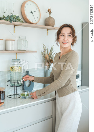 キッチンカウンターでウォーターサーバーからデトックスウォーターを注ぐ女性 キッチンカウンターでウォーターサーバーからデトックスウォーターを注ぐ女性 137278934