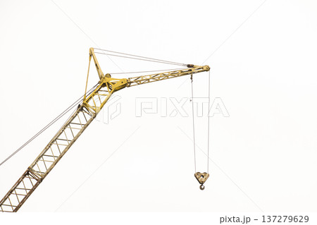 A professional yellow lattice boom crane with a steel hook suspended against a neutral bright background. This minimalist industrial shot emphasizes the power and scale of modern engineering machinery 137279629