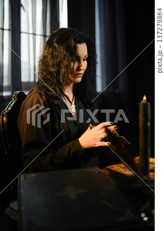Woman reads tarot cards in a dimly lit room with candles and curtains during the evening Woman reads tarot cards in a dimly lit room with candles and curtains during the evening 137279864