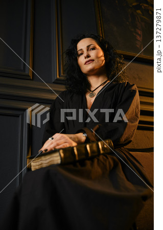 Woman holding a book in a dark room with elegant wall details and soft lighting 137279871