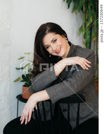 A beautiful smiling brunette poses while sitting on a chair. Businesswoman. Plus-size model. Happy woman concept.  137280649