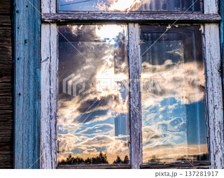 Setting sun and curly clouds reflected in an old rustic window Setting sun and curly clouds reflected in an old rustic window 137281917