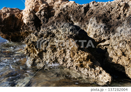 A large rock formation on the shore of a red sea. A weathered limestone cliff on a crystal-clear seashore with calm blue water. Egypt. 137282004