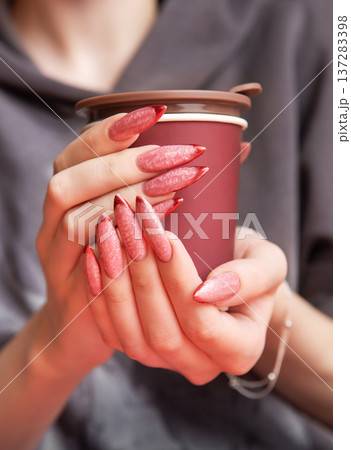 Woman holding insulated cup with long red ombre manicure Woman holding insulated cup with long red ombre manicure 137283398