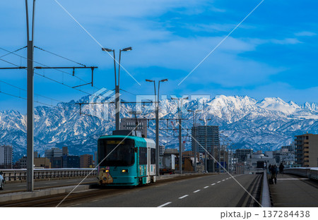 雪の立山連峰を背景に富山市呉羽橋を渡る路面電車 137284438