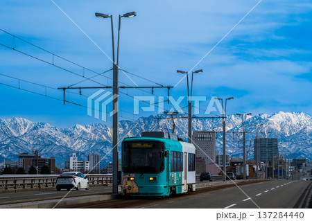 雪の立山連峰を背景に富山市呉羽橋を渡る路面電車 137284440