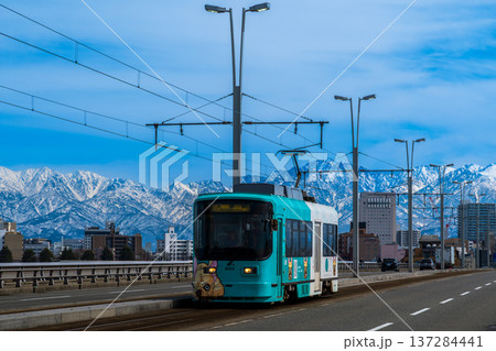 雪の立山連峰を背景に富山市呉羽橋を渡る路面電車 137284441