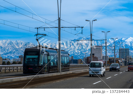 雪の立山連峰を背景に富山市呉羽橋を渡る路面電車 137284443