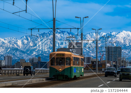 雪の立山連峰を背景に富山市呉羽橋を渡る路面電車 137284444