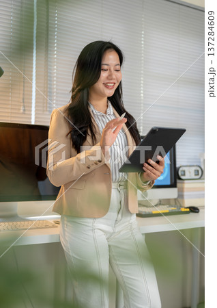 Pretty asian businesswoman office worker holding stylus looking at tablet standing at computer table Pretty asian businesswoman office worker holding stylus looking at tablet standing at computer table 137284609