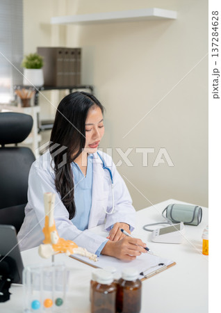 Young asian woman doctor talking while holding pen over clipboard at working table in diagnosis room 137284628