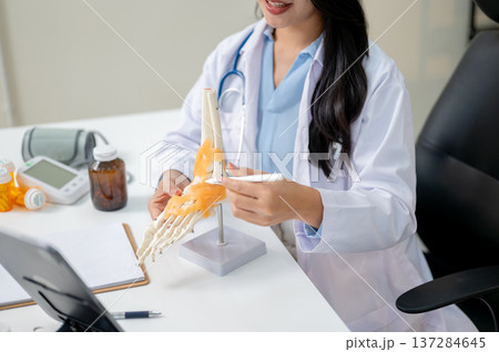 Close up woman doctor teaching or explaining bone model on video call in tablet on diagnosis table. 137284645
