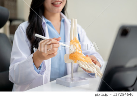 Close up of woman doctor teaching explaining bone model to video call in tablet on diagnosis table. 137284646
