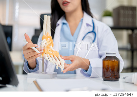 Close up of a woman doctor explaining bone model to tablet aside medicine bottle at diagnosis table. Close up of a woman doctor explaining bone model to tablet aside medicine bottle at diagnosis table. 137284647