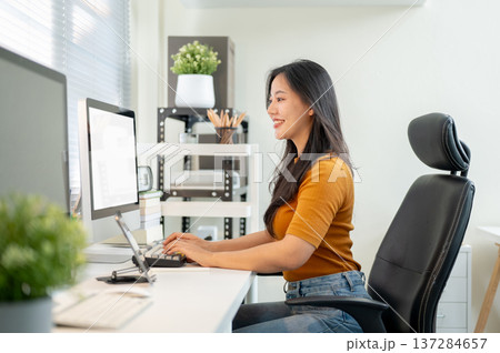 Pretty asian woman freelancer or office worker typing on computer sitting at table in company room. Pretty asian woman freelancer or office worker typing on computer sitting at table in company room. 137284657