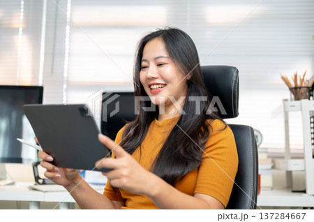 Asian woman freelancer office worker looking watching on tablet sitting on leather chair in company. 137284667