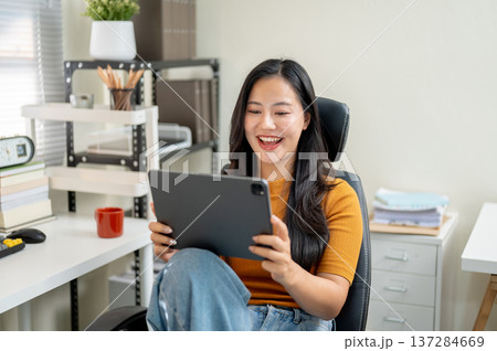Asian woman freelancer or office worker watching video on tablet sitting on leather chair at company Asian woman freelancer or office worker watching video on tablet sitting on leather chair at company 137284669