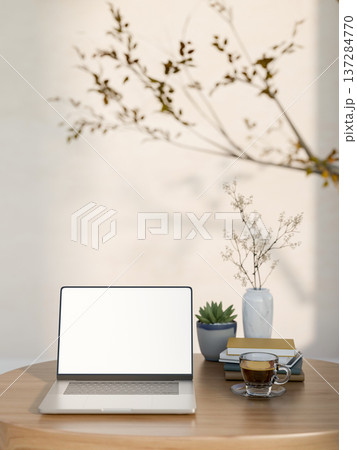 White screen laptop with books and coffee on wooden tale with decors tree branch aside plain wall. 137284770