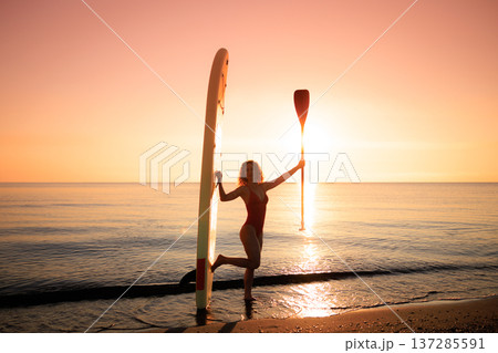 Young woman standing with stand up paddle sup boards by the sea during summer vacation Young woman standing with stand up paddle sup boards by the sea during summer vacation 137285591