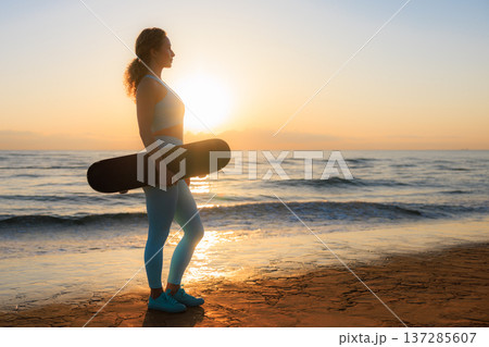 Fit young woman is posing against sea background. Sporty female with skateboard on the seaside promenade. Fit young woman is posing against sea background. Sporty female with skateboard on the seaside promenade. 137285607