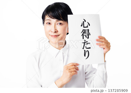 心得たりと書かれた紙を持ち微笑む白いシャツを着たシニア女性 137285909