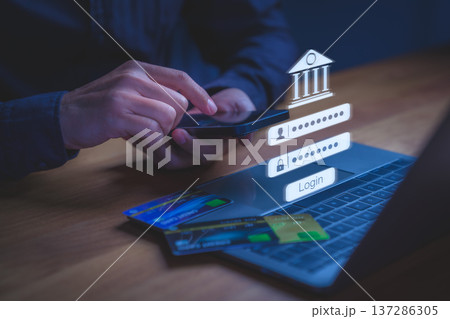 User accessing online banking through smartphone with digital login credential displayed above a laptop, symbolizing secure transaction, financial technology, authentication, and digital banking. User accessing online banking through smartphone with digital login credential displayed above a laptop, symbolizing secure transaction, financial technology, authentication, and digital banking. 137286305
