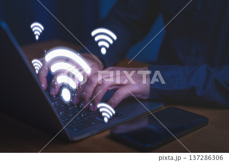 Person using laptop computer with Wi-Fi icons symbolizes wireless connectivity, high speed internet access, digital communication, network technology, and modern online work environments. 137286306