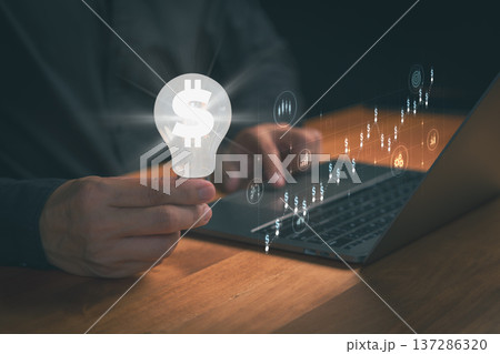 Person holding a lightbulb with a dollar symbol beside a laptop, representing financial innovation, investment ideas, digital business growth, creative money strategies, and economic opportunities. Person holding a lightbulb with a dollar symbol beside a laptop, representing financial innovation, investment ideas, digital business growth, creative money strategies, and economic opportunities. 137286320