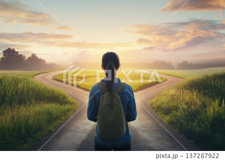 Woman Standing at a Crossroad in a Scenic Landscape during Sunrise with Lush Green Fields 137287922