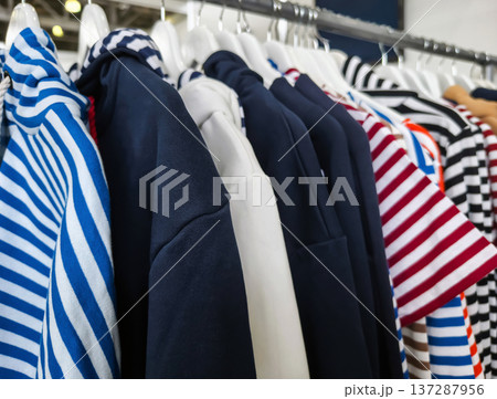 Clothes and vests hanging on a rack in a store showing various striped patterns and colors during daylight Clothes and vests hanging on a rack in a store showing various striped patterns and colors during daylight 137287956