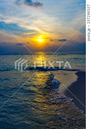 Golden sun sets over calm ocean waves 137290327