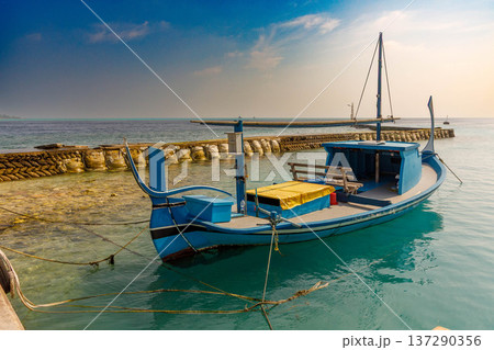 Blue fishing boat rests calm by stone breakwater Blue fishing boat rests calm by stone breakwater 137290356