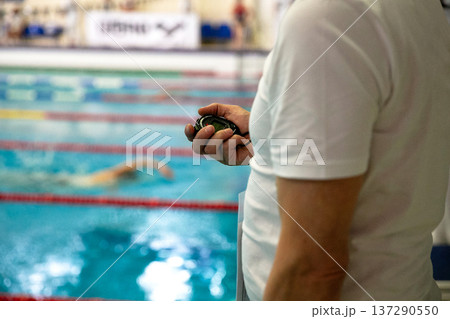 Swimming coach stands poolside holding stopwatch 137290550