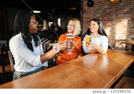Diverse women friends enjoying beer and toasting at a bar Diverse women friends enjoying beer and toasting at a bar 137290576