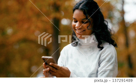 Indian woman smiling using smartphone in autumn park 137291489