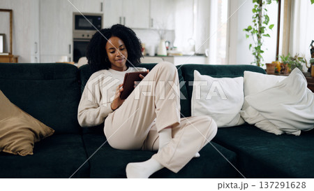 Young black woman relaxing on sofa using tablet 137291628