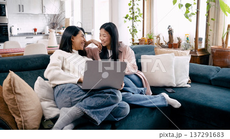 Young women friends relaxing on sofa using laptop Young women friends relaxing on sofa using laptop 137291683