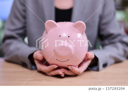 Holding a cheerful pink piggy bank symbolizes savings and financial security in a modern office setting Holding a cheerful pink piggy bank symbolizes savings and financial security in a modern office setting 137293204