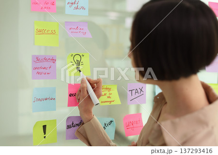 Busy professional organizing tasks with colorful sticky notes during a productive work session in a bright office space Busy professional organizing tasks with colorful sticky notes during a productive work session in a bright office space 137293416
