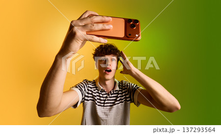 Young man taking selfie with smartphone on yellow green gradient background. Young man taking selfie with smartphone on yellow green gradient background. 137293564
