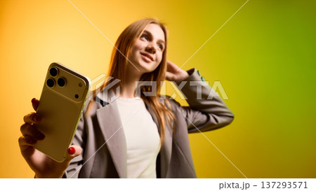 Business woman holding smartphone toward camera on yellow green gradient background Business woman holding smartphone toward camera on yellow green gradient background 137293571