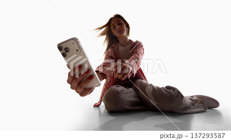 Young woman sitting on floor using smartphone isolated on white background. 137293587