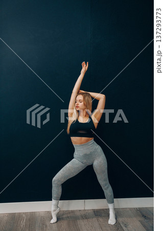 Young woman stretches her body against a wall in activewear as part of her fitness routine, smiling while exercising for health and well-being. Young woman stretches her body against a wall in activewear as part of her fitness routine, smiling while exercising for health and well-being. 137293773