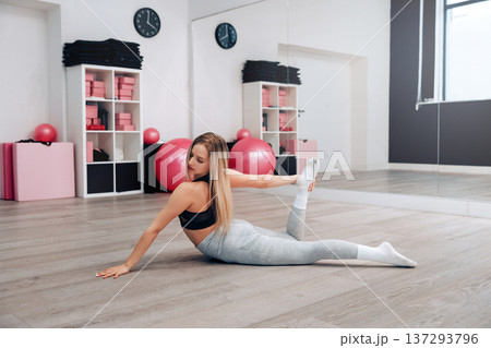 Young Female Practices Seated Side Stretch Exercise In Indoor Gym Space Focusing On Health. Girl Stretching, Enjoying Fitness Training Yoga. Young Female Practices Seated Side Stretch Exercise In Indoor Gym Space Focusing On Health. Girl Stretching, Enjoying Fitness Training Yoga. 137293796