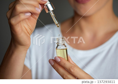 Close up beauty portrait of a beautiful woman with glowing skin is applying a vitamin C skincare product with a pipette dropper. Serum 137293811