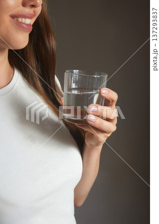 Close up smiling young woman holding glass of clean mineral water,. Young woman drinks a glass of water. Close up smiling young woman holding glass of clean mineral water,. Young woman drinks a glass of water. 137293837